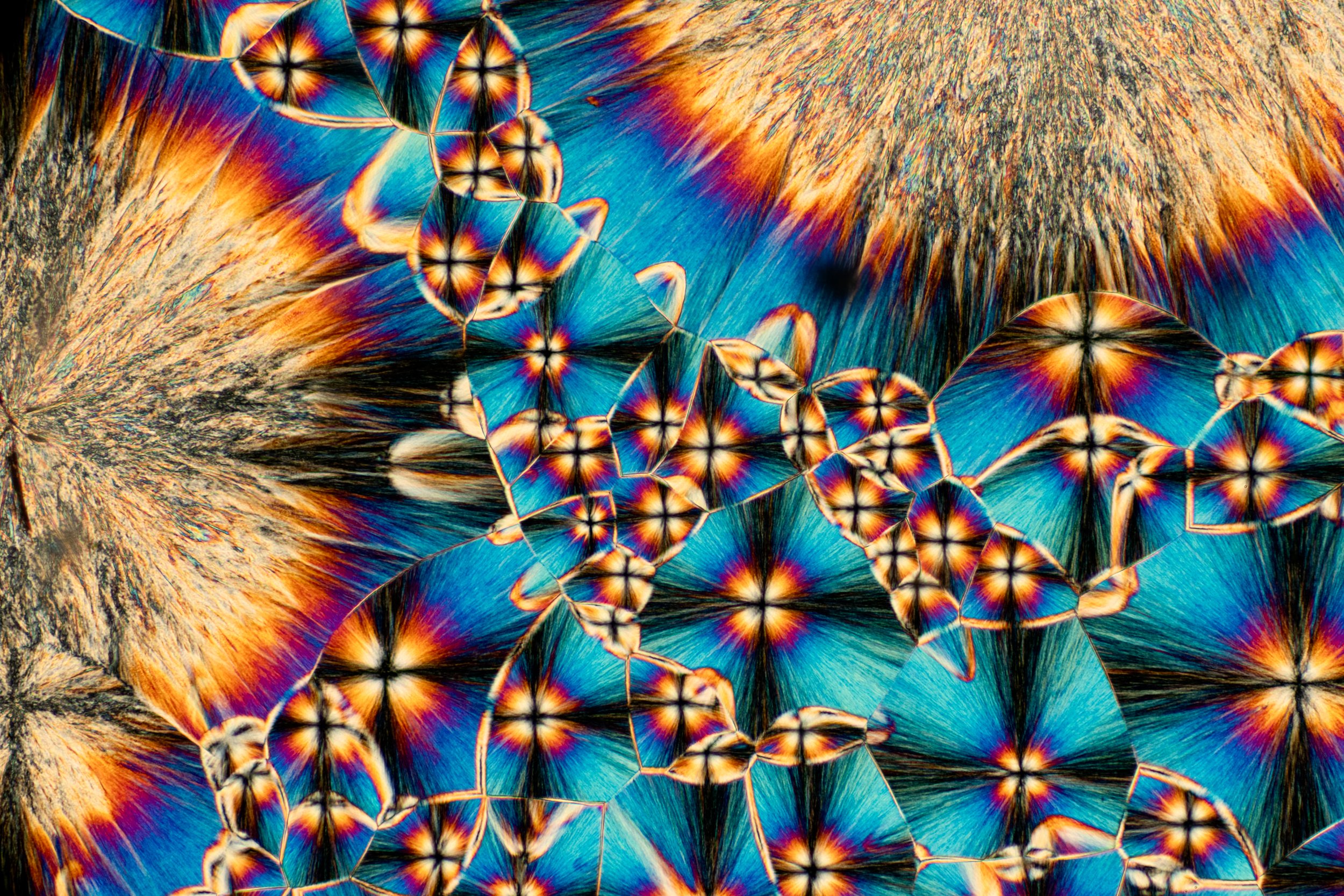 Microscopic cross-polarization of ice, colorful with vibrant blue, orange, and black patterns and a textured surface.