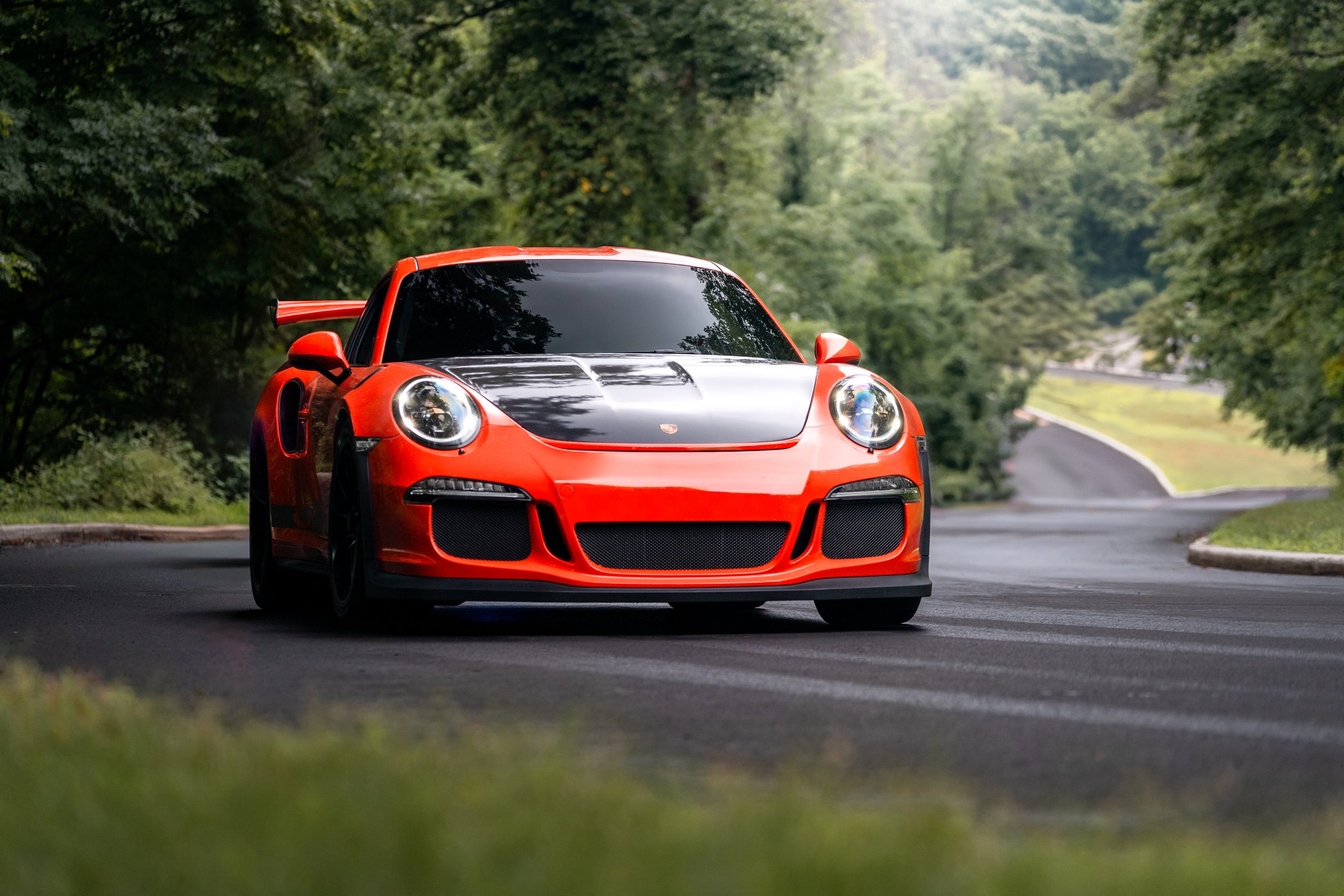 A red and black Porsche GT3rs driving on a winding road surrounded by green trees.