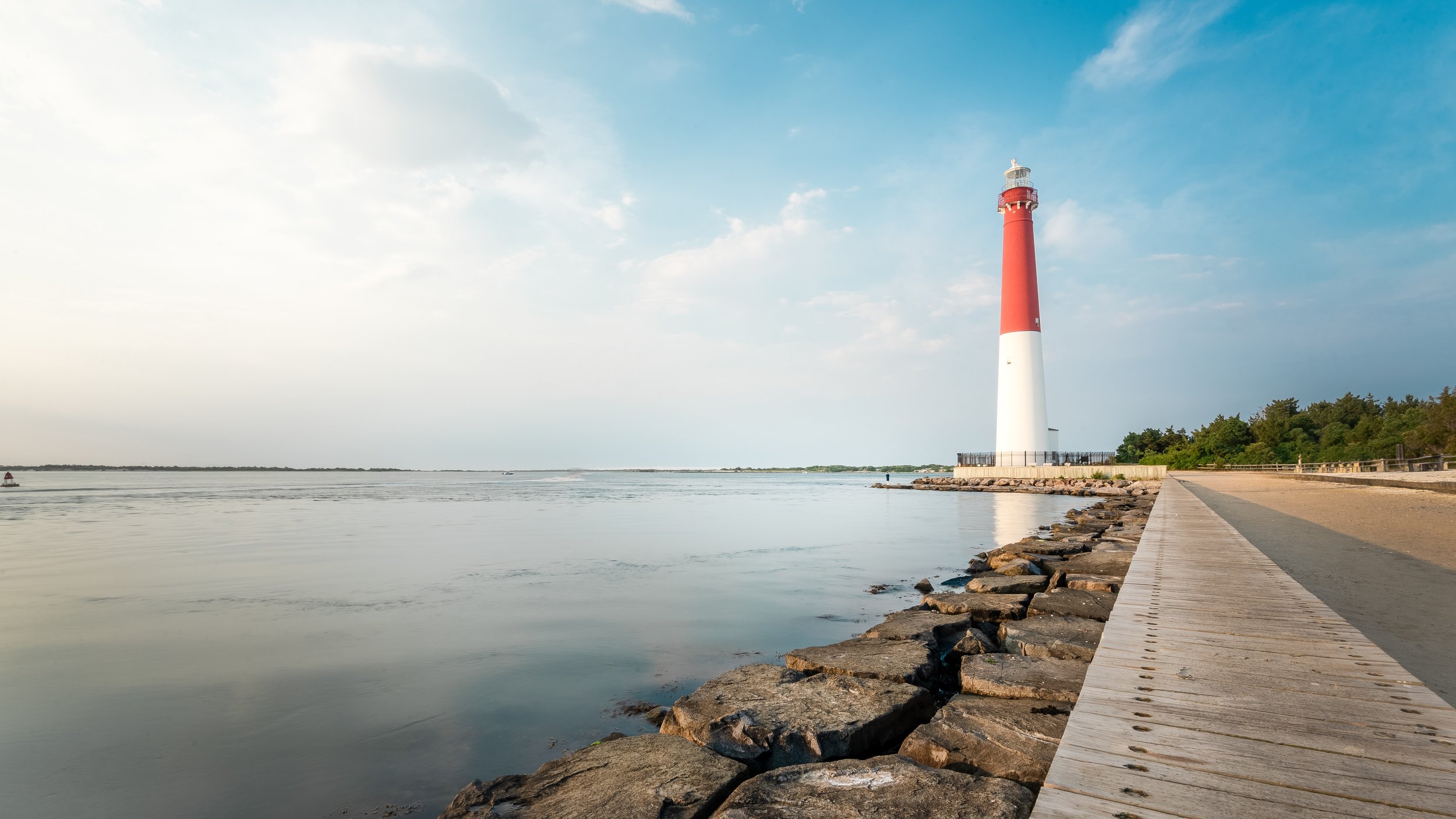 A lighthouse near the water on a clear day with a stone and wooden pathway along the shoreline at Long Beach Island