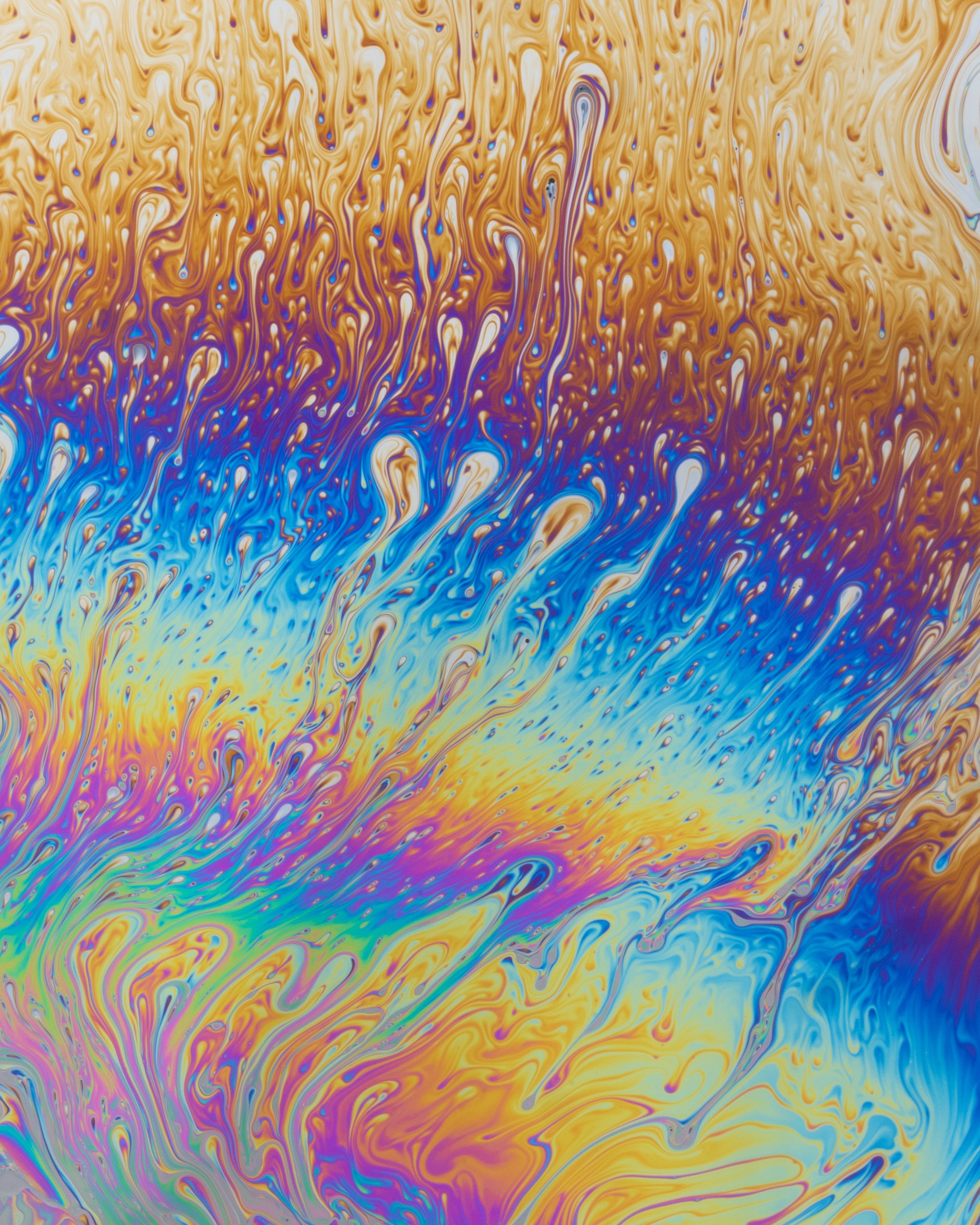 Swirling soap bubbles at macro scale with shades of brown, blue, orange, yellow, pink, and purple.